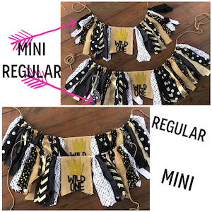 May include: Two burlap banners with the text "Wild One" in black lettering and a gold crown. The banners are decorated with black, white, and gold fabric scraps. The smaller banner is labelled "mini" and the larger banner is labelled "regular".