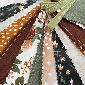 May include: A bunting banner with a scalloped edge, featuring a variety of fabric patterns in shades of brown, green, and white. The fabric patterns include polka dots, floral designs, and solid colors.