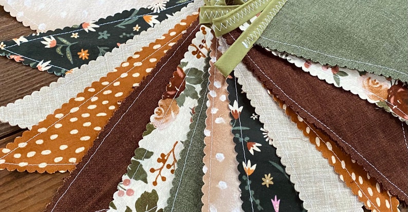 May include: A bunting banner with a scalloped edge, featuring a variety of fabric patterns in shades of brown, green, and white. The fabric patterns include polka dots, floral designs, and solid colors.
