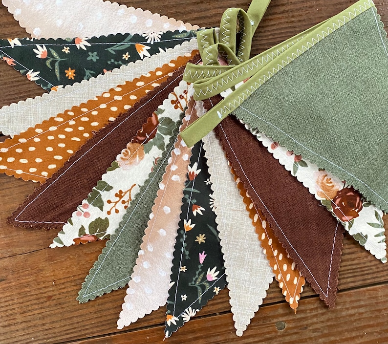 May include: A bunting banner with 12 triangular flags in various shades of brown, green, and white. The flags are decorated with different patterns, including polka dots, floral designs, and solid colors. The bunting is perfect for adding a touch of rustic charm to any party or event.
