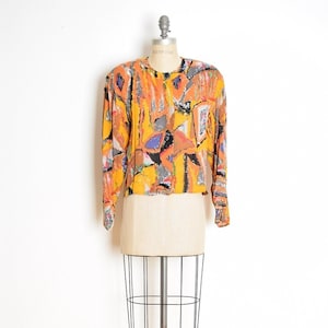May include: A yellow, orange, black, and blue abstract print blouse with long sleeves and a button-up front.