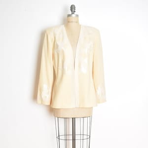 May include: A cream-colored blazer with white beaded embellishments on the front and sleeves. The blazer is on a dress form.
