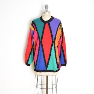 May include: A vintage sweater with a geometric pattern in red, pink, green, blue, purple, and orange. The sweater has a black crew neck and black trim. The sweater is displayed on a vintage dress form.