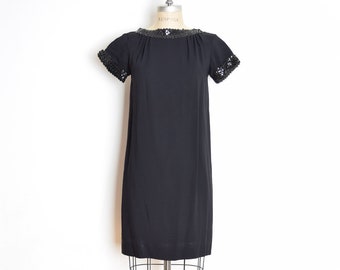 May include: A black short-sleeved dress with a sequined neckline and cuffs. The dress is on a mannequin.