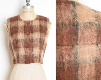 May include: A vintage, cropped vest in a plaid pattern of brown, peach, and muted green. The vest has a round neckline, three brown buttons, and a fuzzy texture. The garment is displayed on a mannequin.