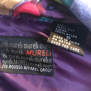 May include: A purple silk jacket with a colorful floral print. The label reads "SHELL: 100% SILK LINING: 100% NYLON MADE IN CHINA RN 45749 S OVER FOR CARE mureli mureli mureli mure Tureli mureli MURELI rell mureli mureli murelin aureli MURELI mureli mure DIV ROUSSO APPAREL GROUP"