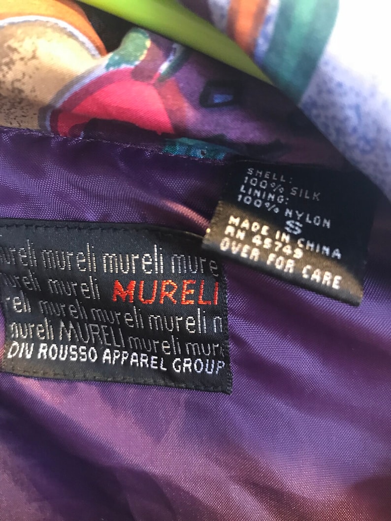 May include: A purple silk jacket with a colorful floral print. The label reads "SHELL: 100% SILK LINING: 100% NYLON MADE IN CHINA RN 45749 S OVER FOR CARE mureli mureli mureli mure Tureli mureli MURELI rell mureli mureli murelin aureli MURELI mureli mure DIV ROUSSO APPAREL GROUP"