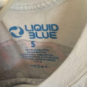 May include: White t-shirt with the blue text "LIQUID BLUE" and the size "S". The shirt's tag also includes washing instructions and the text "100% PRE-SHRUNK COTTON".