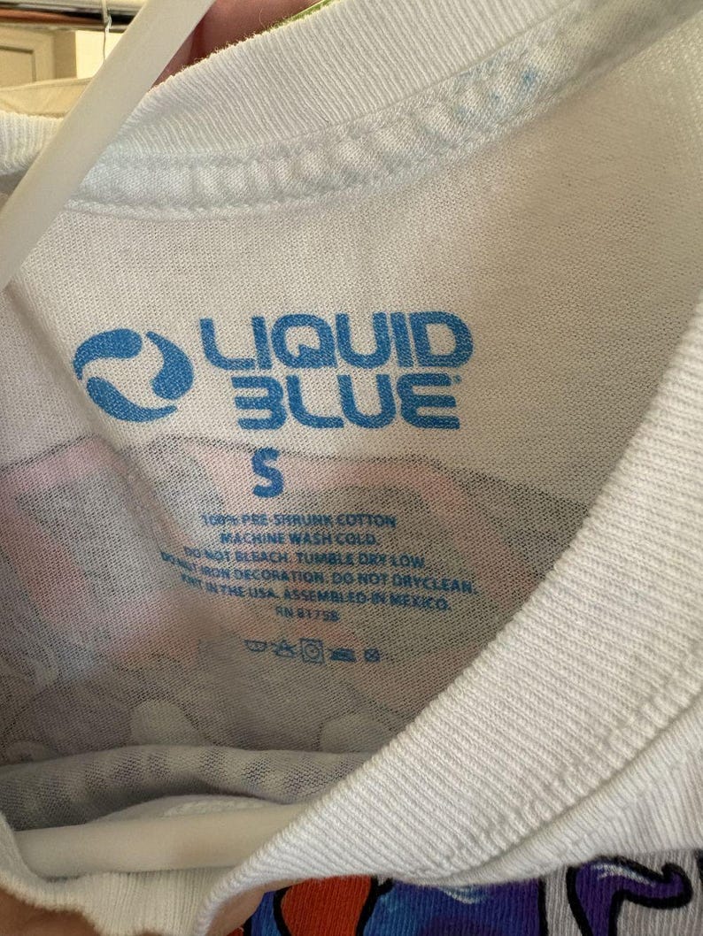 May include: White t-shirt with the blue text "LIQUID BLUE" and the size "S". The shirt's tag also includes washing instructions and the text "100% PRE-SHRUNK COTTON".