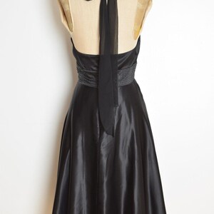 May include: A black satin halter dress with a beaded waistline and a flowing skirt. The dress features a long, sheer tie that drapes down the back. The dress is displayed on a mannequin.