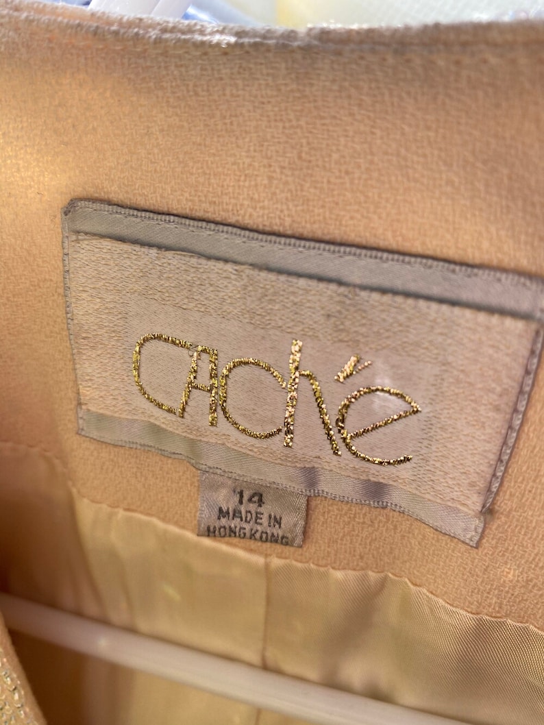 May include: A beige jacket with a white label that says "ache" in gold lettering. The label also says "14" and "Made in Hong Kong".