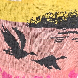 May include: A knitted sweater with a multi-colored design. The sweater features a yellow and white striped pattern at the top, a pink section with a black bird design, and a pink section with a pink floral pattern at the bottom.