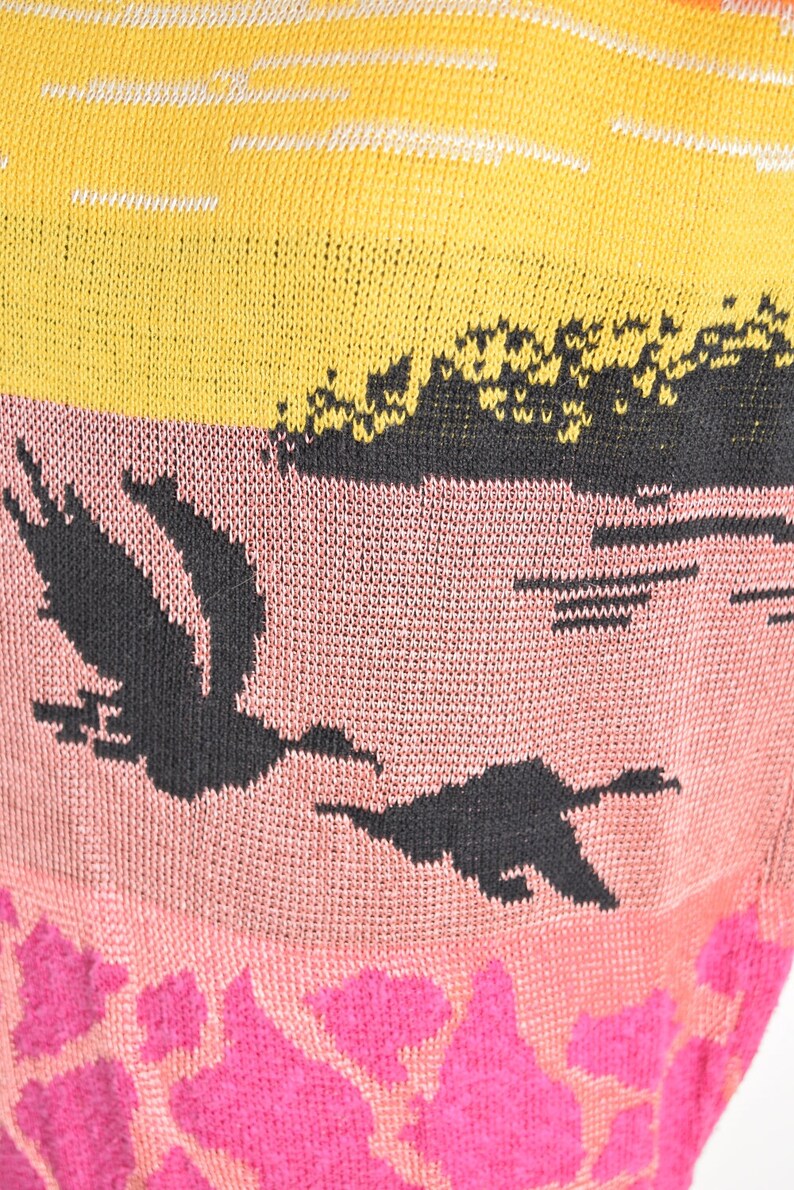May include: A knitted sweater with a multi-colored design. The sweater features a yellow and white striped pattern at the top, a pink section with a black bird design, and a pink section with a pink floral pattern at the bottom.