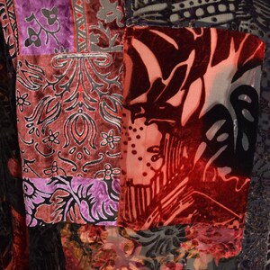 May include: Close-up of a patchwork garment featuring various patterned velvet fabrics. The colors include deep reds, purples, and blacks, with floral and abstract designs. The garment appears to be a jacket or coat.