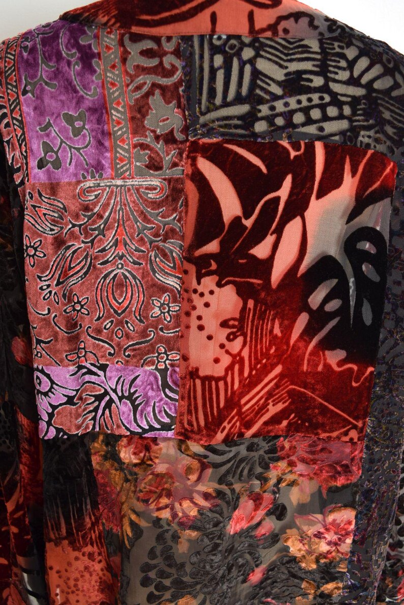 May include: Close-up of a patchwork garment featuring various patterned velvet fabrics. The colors include deep reds, purples, and blacks, with floral and abstract designs. The garment appears to be a jacket or coat.