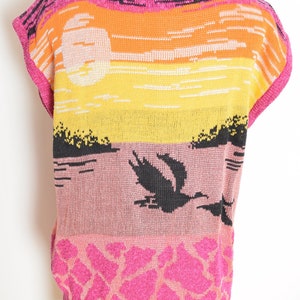 May include: A pink sleeveless sweater with a sunset and birds design. The sweater has a black, orange, yellow, and pink color scheme.