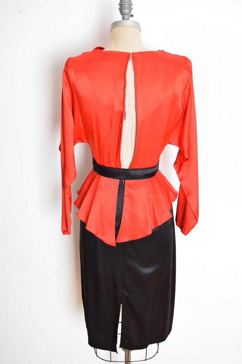 May include: A red and black dress with a fitted skirt and a peplum top. The dress has a keyhole back and a black belt.