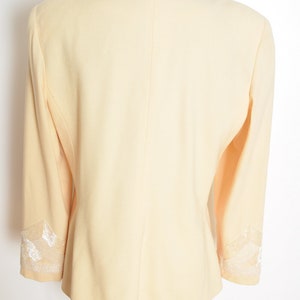 May include: A pale yellow blazer with white lace trim on the collar and cuffs.