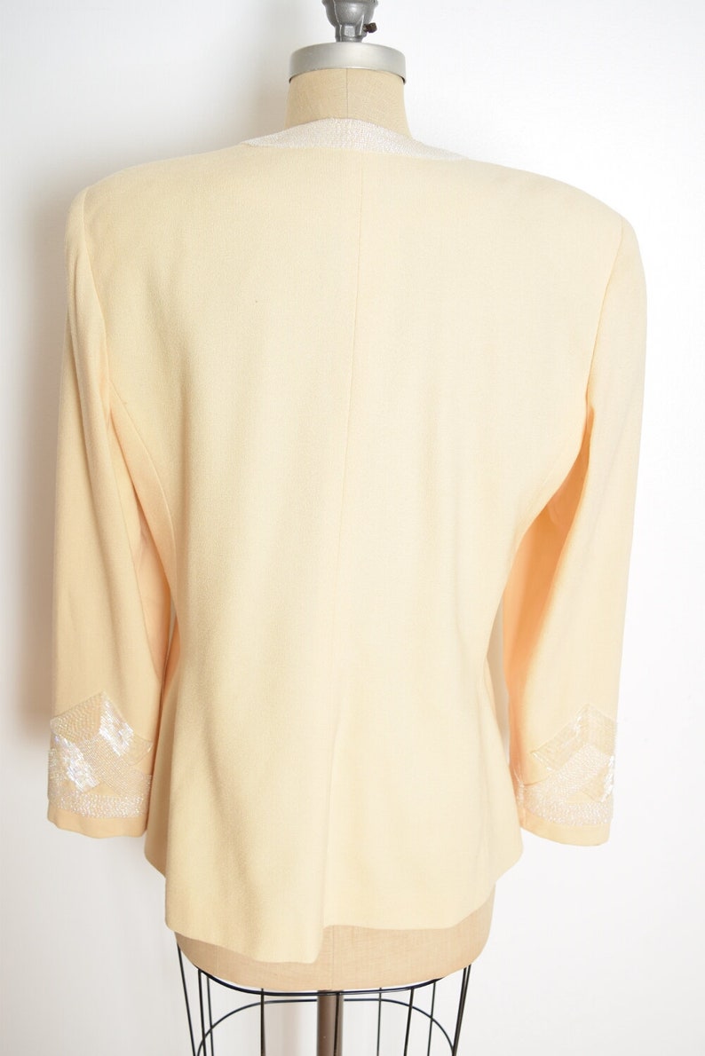 May include: A pale yellow blazer with white lace trim on the collar and cuffs.