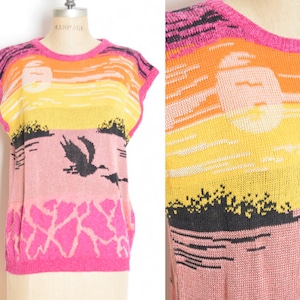 May include: A pink, yellow, and orange sleeveless sweater with a sunset and bird design. The sweater is knitted and has a crew neck.