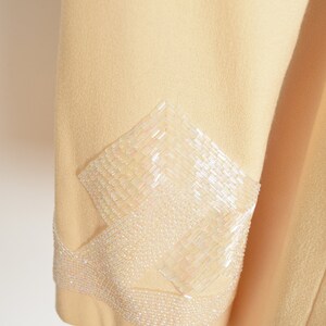 May include: A pale yellow jacket with a decorative beaded design on the sleeve. The beads are white and iridescent.