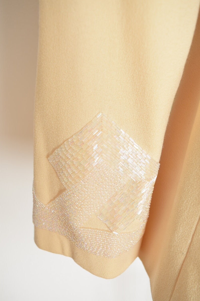 May include: A pale yellow jacket with a decorative beaded design on the sleeve. The beads are white and iridescent.