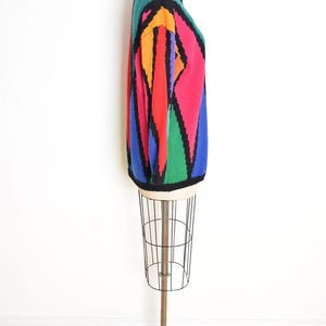 May include: A colorful, geometric-patterned sweater displayed on a mannequin. The sweater features a vibrant design with red, orange, green, blue, and black diamond shapes. The sweater is a long-sleeved, crew-neck style.