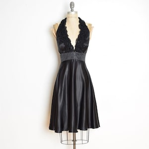 May include: A black satin halter dress with a flared skirt. The bodice features a ruffled neckline and a beaded waist. The dress is displayed on a mannequin against a white background. The dress is knee-length.