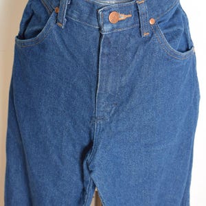 May include: Close-up of blue denim jeans. The jeans have a high waist, copper-colored rivets, and a button closure. The pockets are visible, and the stitching is in a contrasting color. The denim appears to be a medium wash.