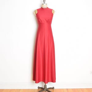 May include: A sleeveless, floor-length red dress displayed on a mannequin. The dress features a high neckline with a decorative trim and a fitted bodice that flows into a full skirt. The dress is made of a smooth, solid fabric.