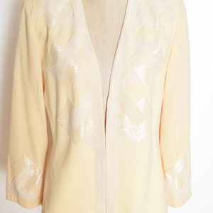 May include: A pale yellow blazer with a V-neck and long sleeves. The blazer is decorated with white beaded geometric designs on the front and cuffs. The label "Rampage" is visible on the mannequin's chest.