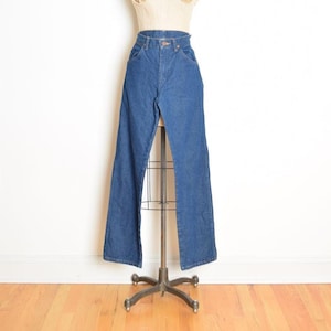 May include: Blue denim jeans with a high waist and flared leg. The jeans are displayed on a mannequin. The denim is a medium wash, and the jeans have classic five-pocket styling. The mannequin is on a metal stand.