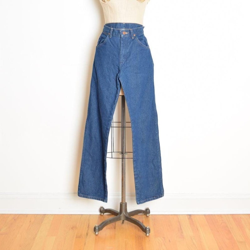 May include: Blue denim jeans with a high waist and flared leg. The jeans are displayed on a mannequin. The denim is a medium wash, and the jeans have classic five-pocket styling. The mannequin is on a metal stand.