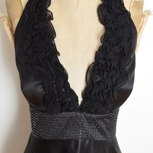 May include: Black halter dress with a ruffled neckline and a beaded waist. The dress is made of a shiny, satin-like material. The dress is displayed on a mannequin.
