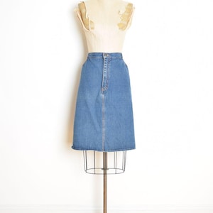 May include: A vintage denim skirt in a light blue wash, displayed on a mannequin. The skirt has a classic A-line silhouette, a button and zipper closure, and a simple, clean design. The skirt is a timeless piece.