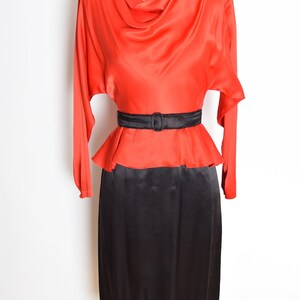 May include: A red and black vintage dress with a cowl neck and a black belt. The dress has long sleeves and a fitted skirt.