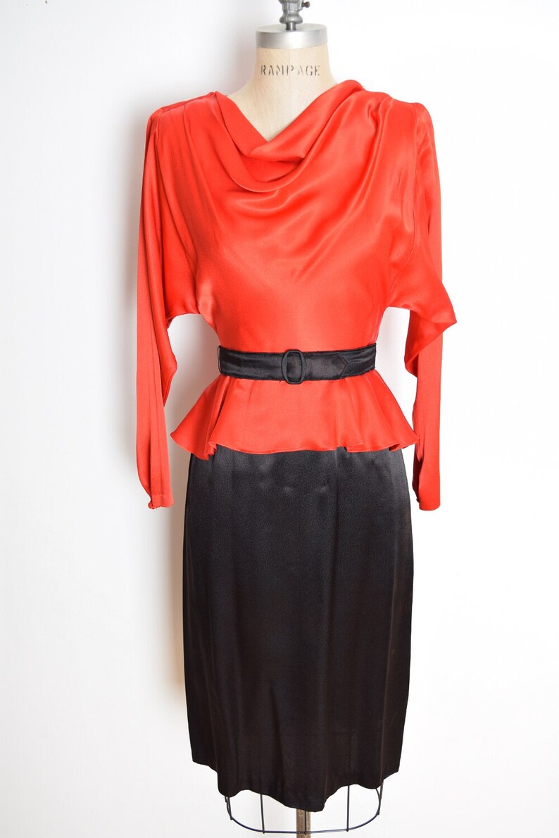 May include: A red and black vintage dress with a cowl neck and a black belt. The dress has long sleeves and a fitted skirt.