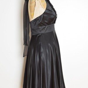 May include: A black satin dress with a halter neckline and a beaded belt. The dress has a flowing skirt and a sheer, draped accent over one shoulder. The dress is displayed on a mannequin.