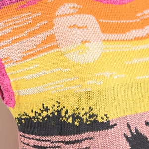 May include: A sleeveless knitted sweater with a colorful sunset design. The sweater is pink, orange, yellow, and black. The design features a sun and a palm tree.
