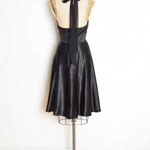 May include: A black satin halter dress displayed on a vintage dress form. The dress features a fitted bodice, a beaded waist detail, and a flowing A-line skirt. A long black tie extends from the halter neckline.