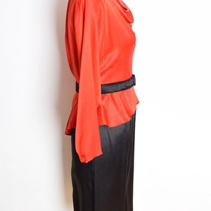 May include: A red and black dress with a cowl neck and a black belt. The dress has long sleeves and a skirt that falls to the knees.