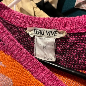 May include: A pink, orange, and black patterned sweater with a white tag that reads "LERU VIVE" and "MADE IN ITALY". The tag also indicates the size "M" and "60% COTONE".