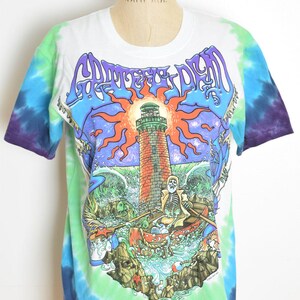 May include: White tie-dye t-shirt with a colorful graphic featuring a lighthouse, skeleton, and boat. The shirt has a crew neck and short sleeves. The graphic includes the text "Grateful Dead" in purple.