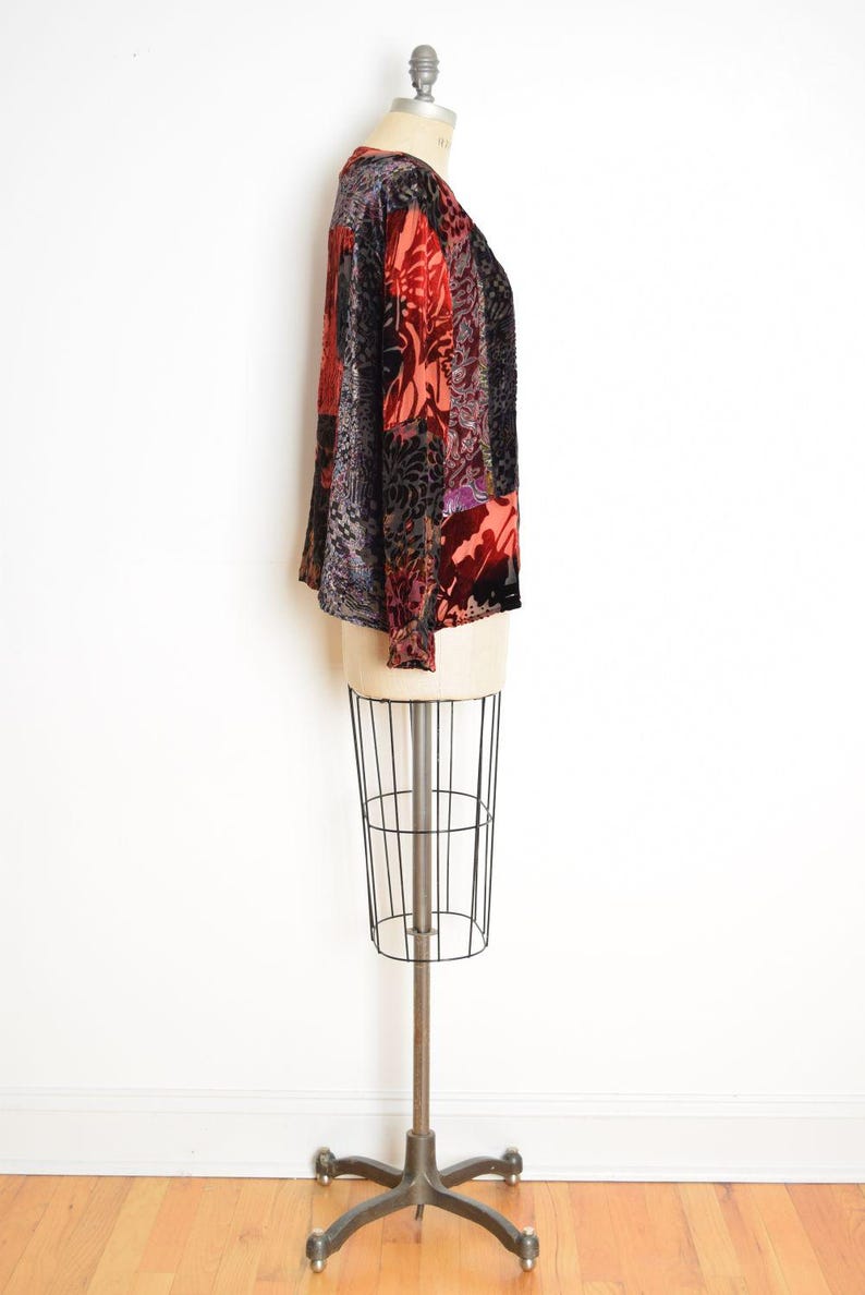 May include: A long-sleeved top with a patchwork design. The top features a mix of patterns and colors, including red, black, and purple. The garment is displayed on a mannequin.