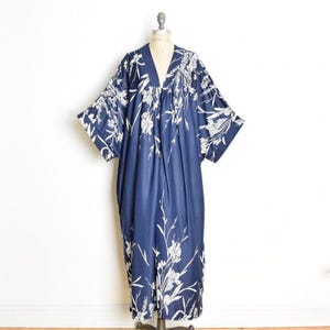 May include: A floor-length navy blue kaftan dress featuring a white floral print. The garment has a V-neckline, wide kimono-style sleeves, and a loose, flowing silhouette that drapes from the shoulders down to the hemline.