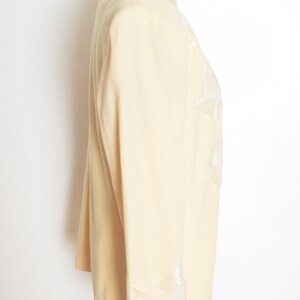 May include: A cream-colored blazer with a white embroidered design on the front and sleeves. The blazer is on a white background.