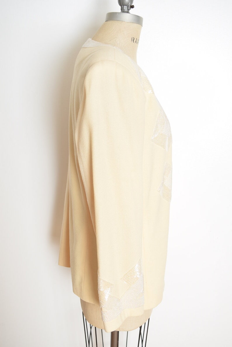 May include: A cream-colored blazer with a white embroidered design on the front and sleeves. The blazer is on a white background.