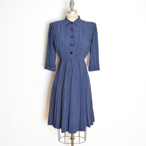 May include: A vintage navy blue dress with white polka dots. The dress features a collared neckline, long sleeves, and a button-down front. The skirt is pleated, and the dress is displayed on a mannequin.