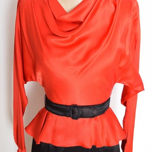 May include: A red satin dress with a cowl neck and a black belt. The dress has a fitted bodice and a flowing skirt.