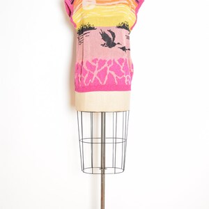 May include: A pink, yellow, and orange sleeveless sweater with a black and white graphic print of a sunset and birds. The sweater is on a mannequin.
